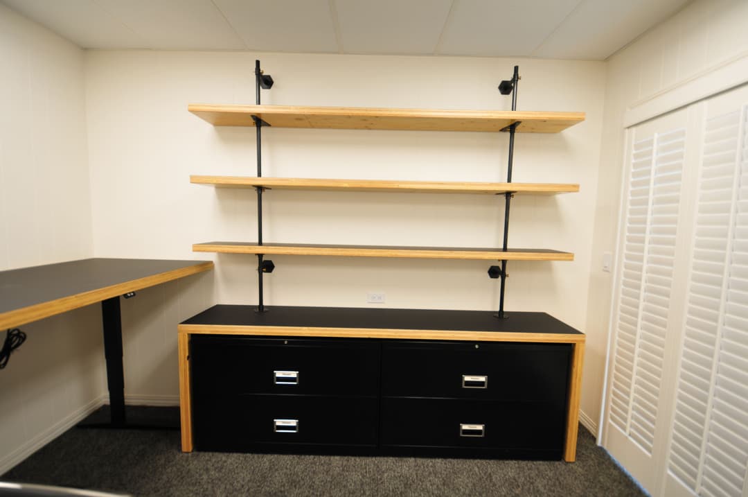 Modern black and wood shelving unit with a desk and drawers in a minimalistic room.