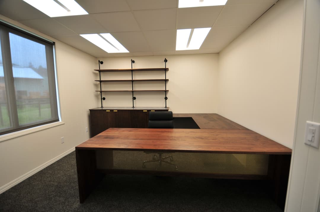 Modern office interior featuring a wooden desk, black chair, and shelving units against a neutral wall.