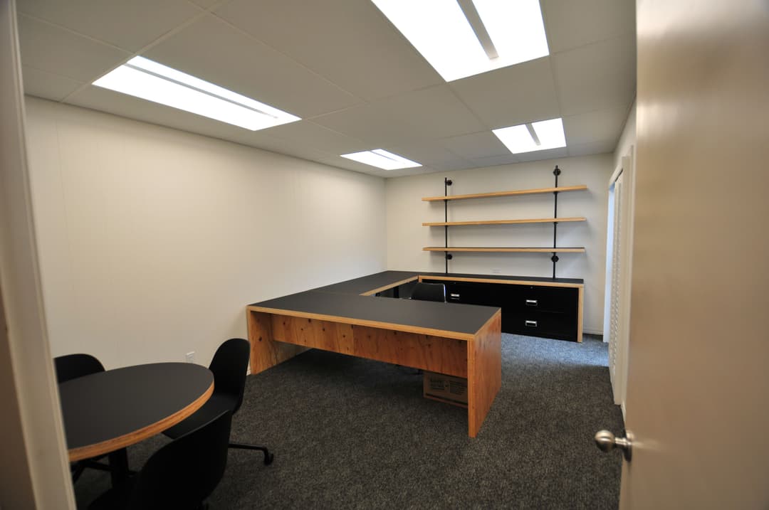 Modern office interior with a large desk, shelves, and circular meeting table on carpet.