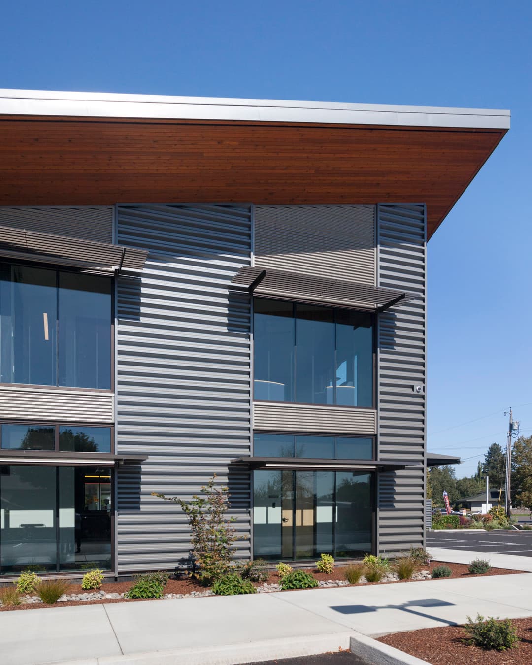 Modern commercial building with sleek metal siding and large windows under a wooden overhang.