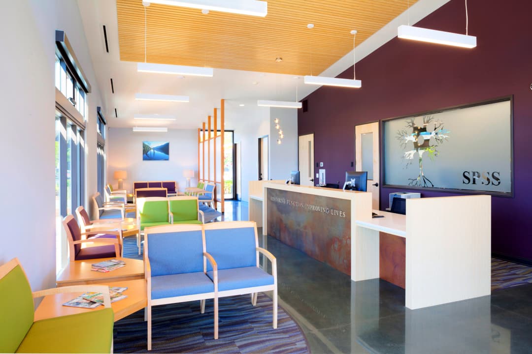 Modern waiting room interior with colorful seating, bright lighting, and reception desk.