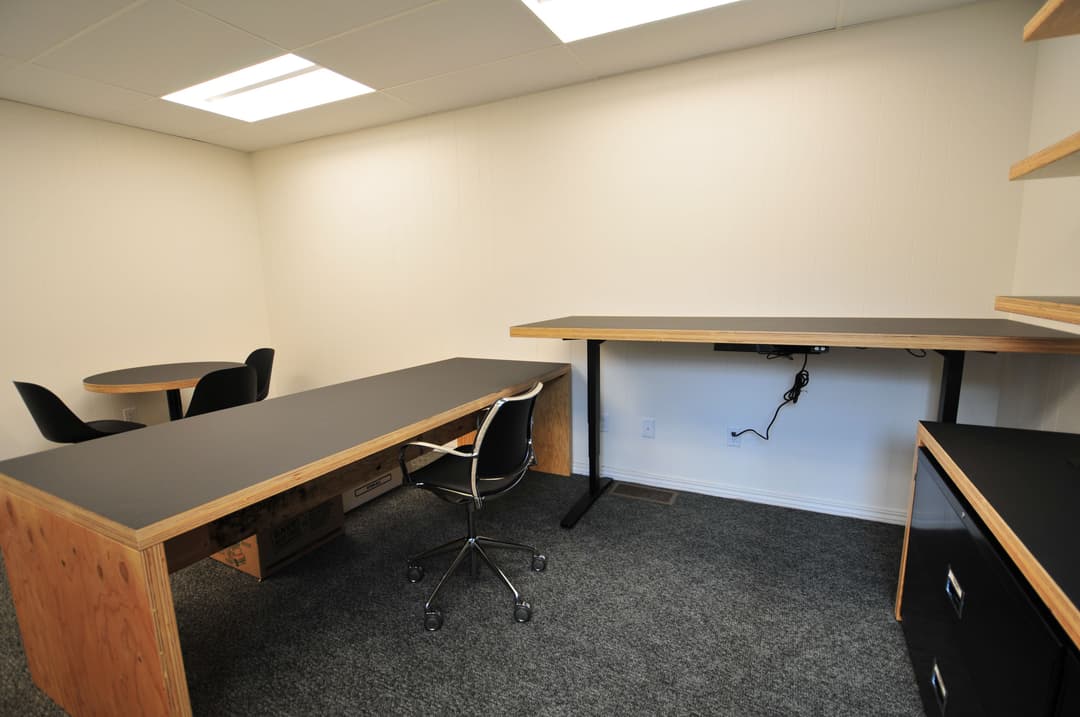 Modern office interior with black desks, chairs, and neutral wall color. Bright lighting above.
