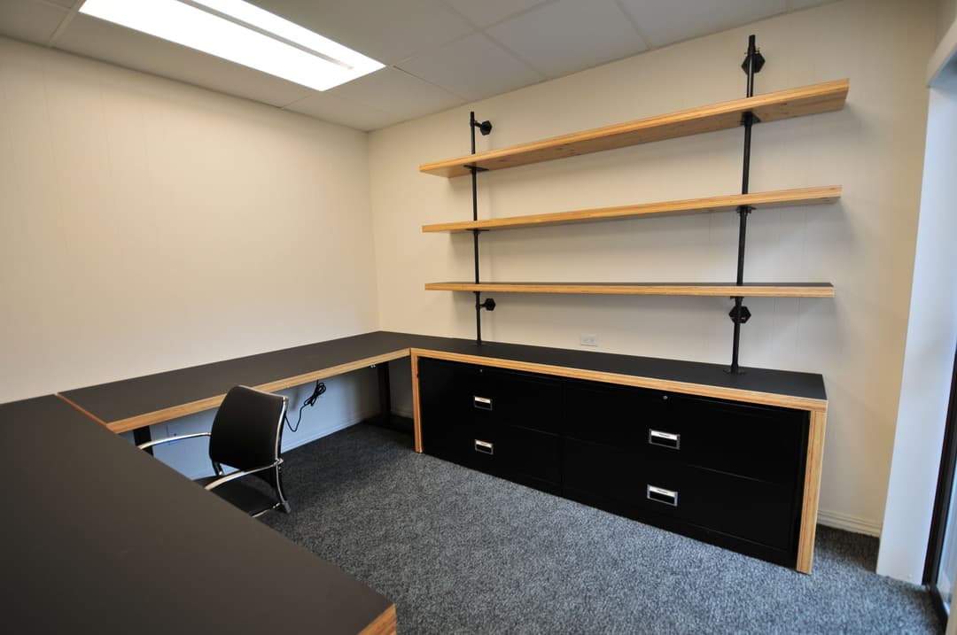 Modern minimalist office workspace with black furniture and wooden shelves.