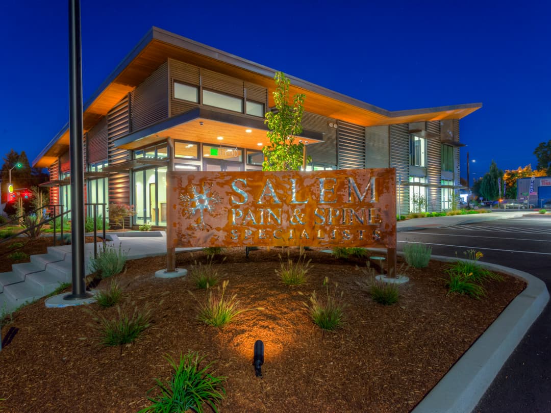 Salem Pain & Spine Specialists building at dusk with illuminated sign and modern architecture.