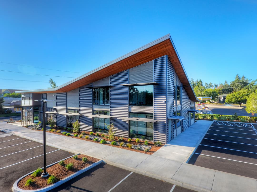 Modern commercial building with large windows and landscaped parking lot. Bright blue sky.