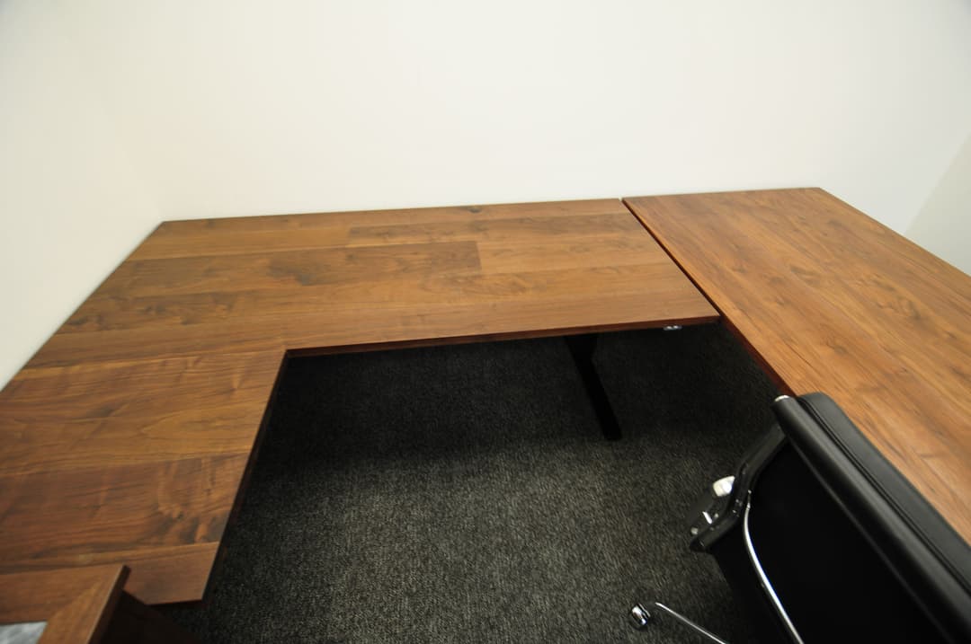L-shaped wooden desk with black office chair in minimalist workspace setting.