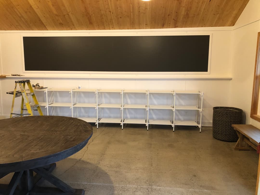 Empty room featuring a large chalkboard, shelving unit, and circular wooden table.