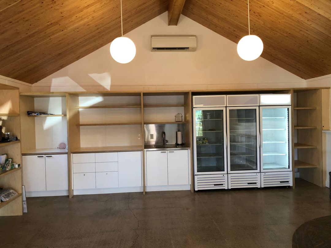 Modern kitchen interior featuring wooden ceiling, shelves, and fridge against smooth concrete floor.