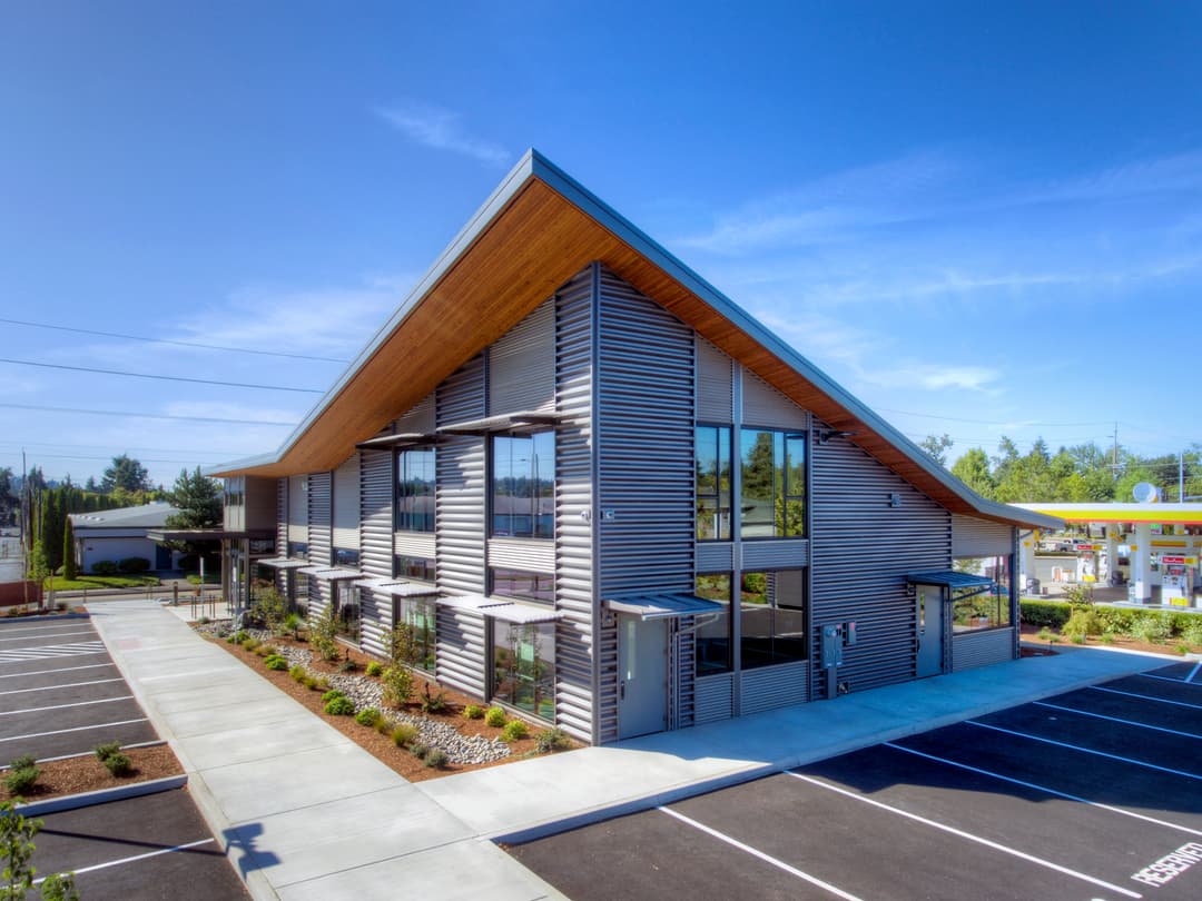 Modern eco-friendly building with wooden accents and large windows, surrounded by parking spaces.