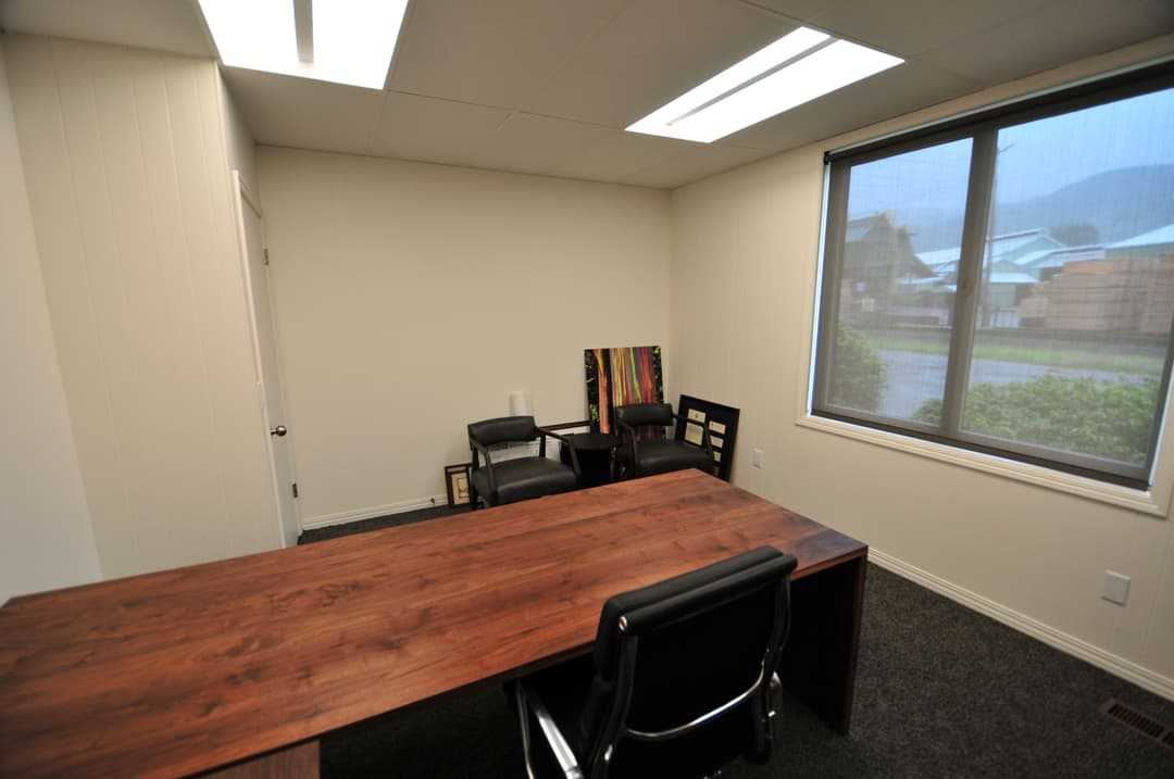Modern office interior featuring a wooden desk, chairs, and large window with natural light.