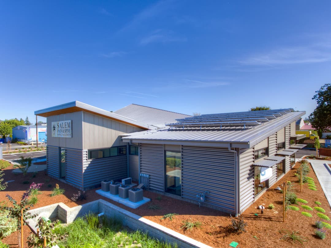 Modern eco-friendly building with solar panels, landscaped garden, and clear blue sky.