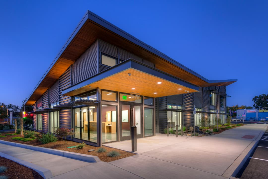 Modern building exterior at dusk with sleek design, glass entrance, and surrounding landscaping.