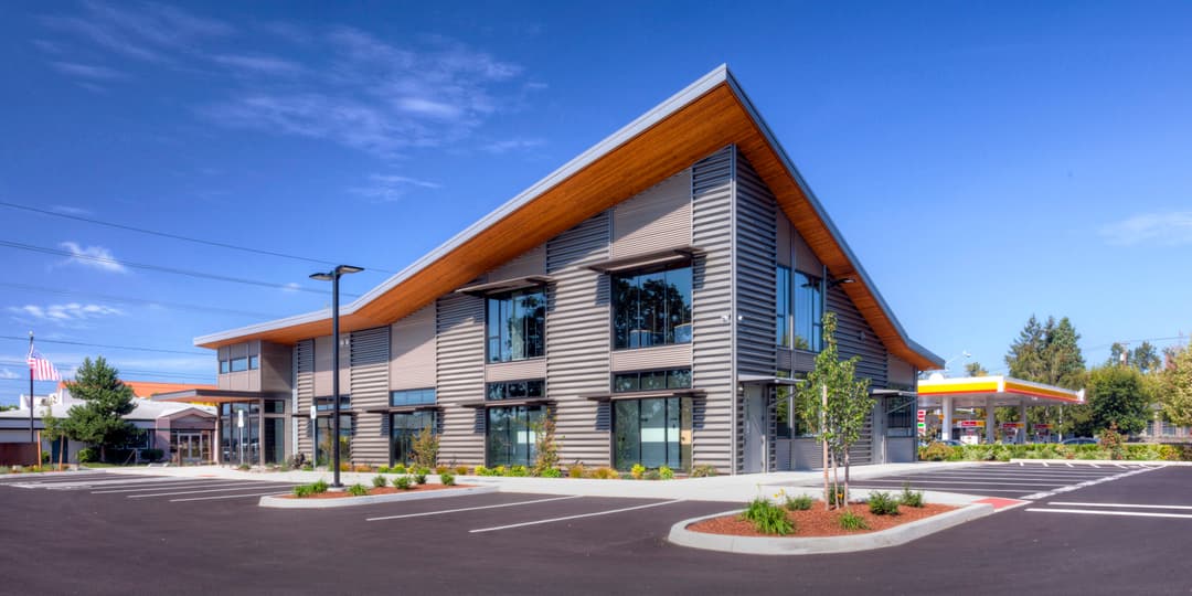 Modern commercial building with large windows, sloped roof, and landscaped parking lot.