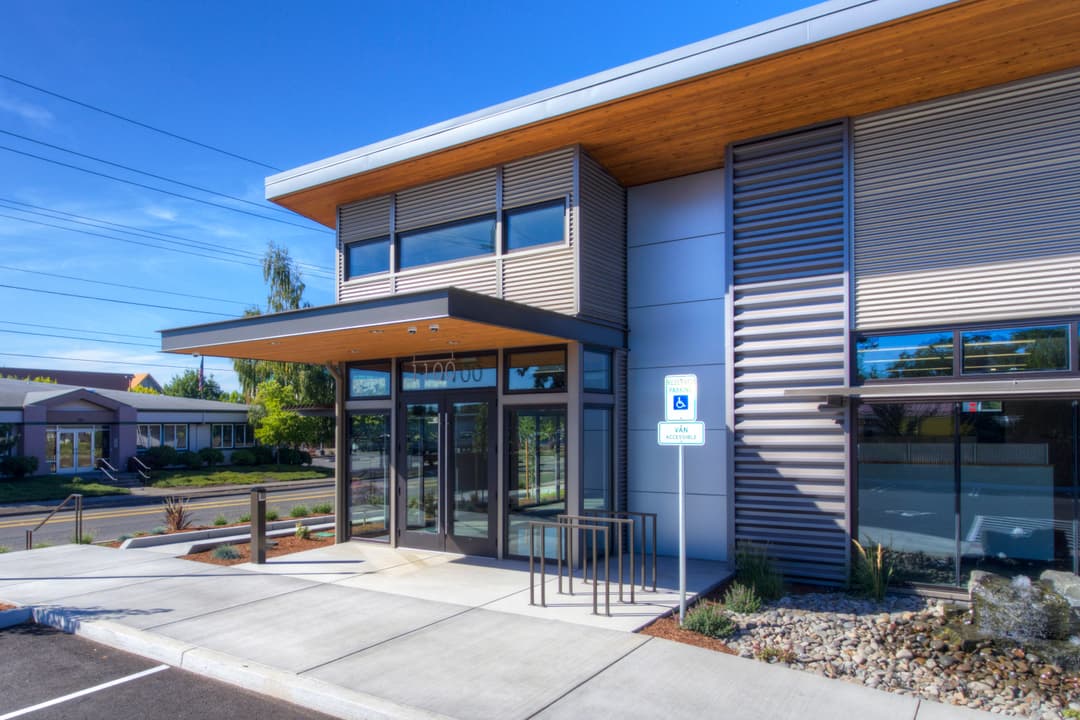 Modern building entrance with accessible parking, bright blue sky, and landscaped surroundings.
