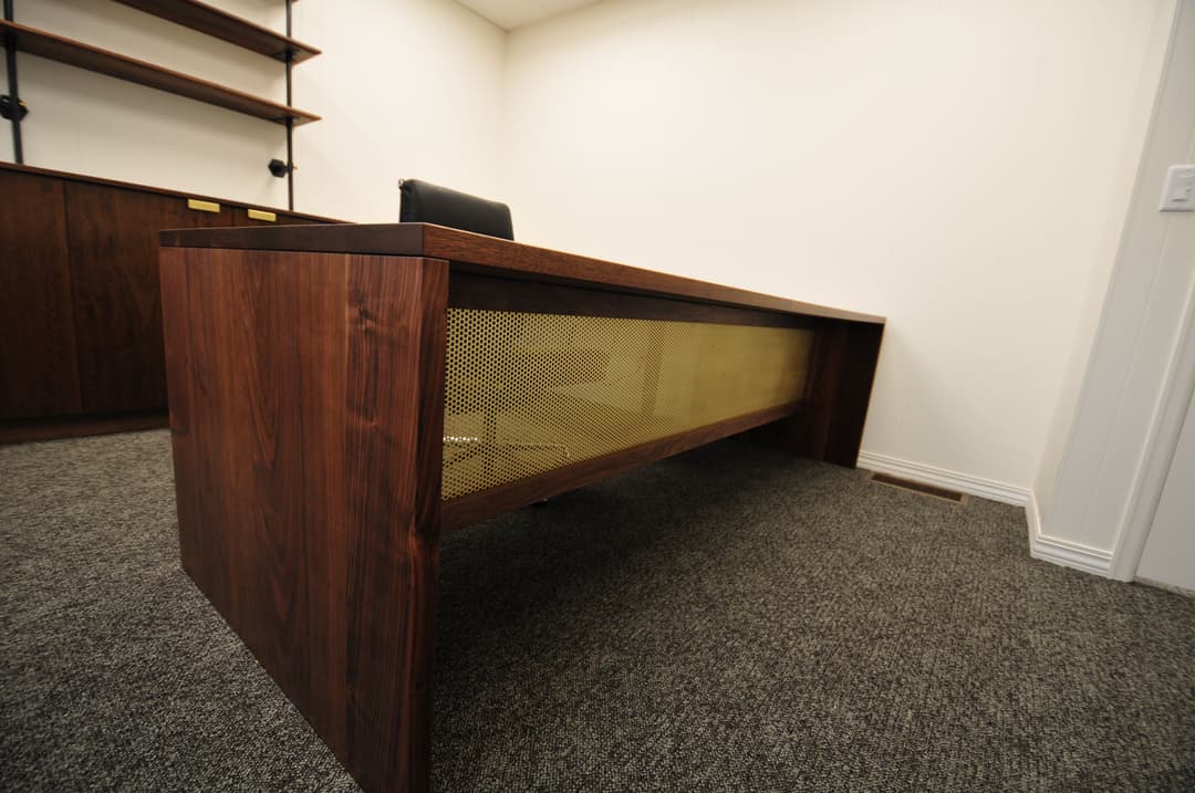 Modern wooden desk with gold mesh detail in sleek office setting.