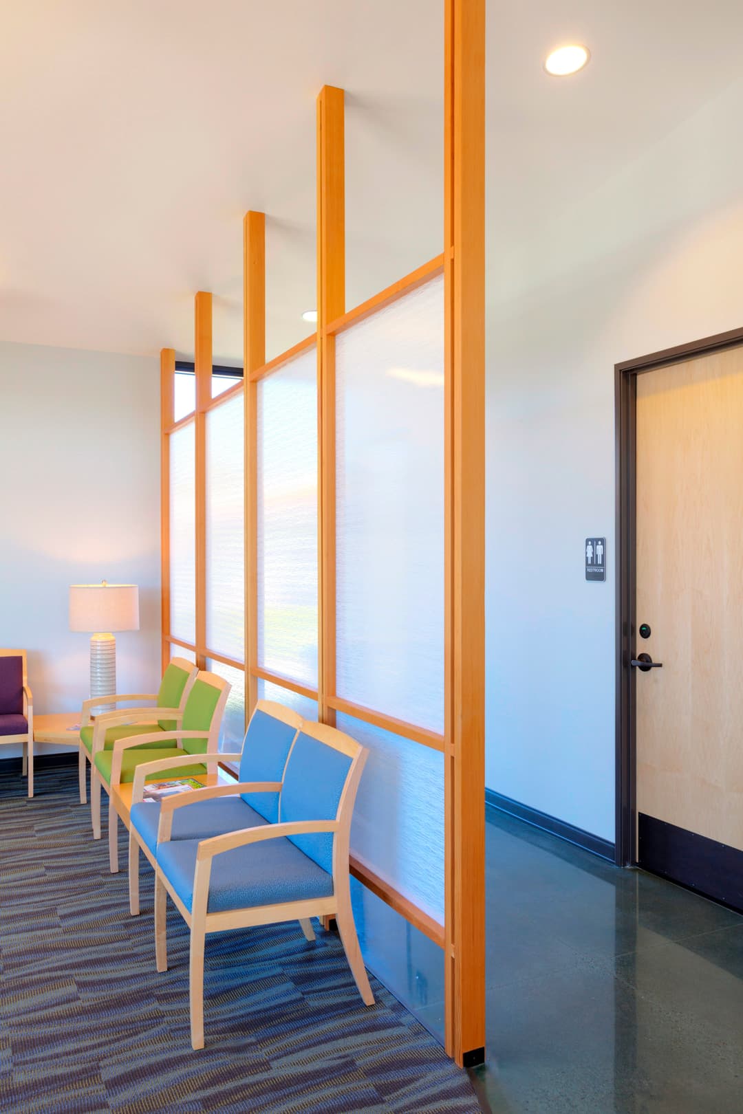 Modern waiting room with colorful chairs, wood accents, and a restroom door.