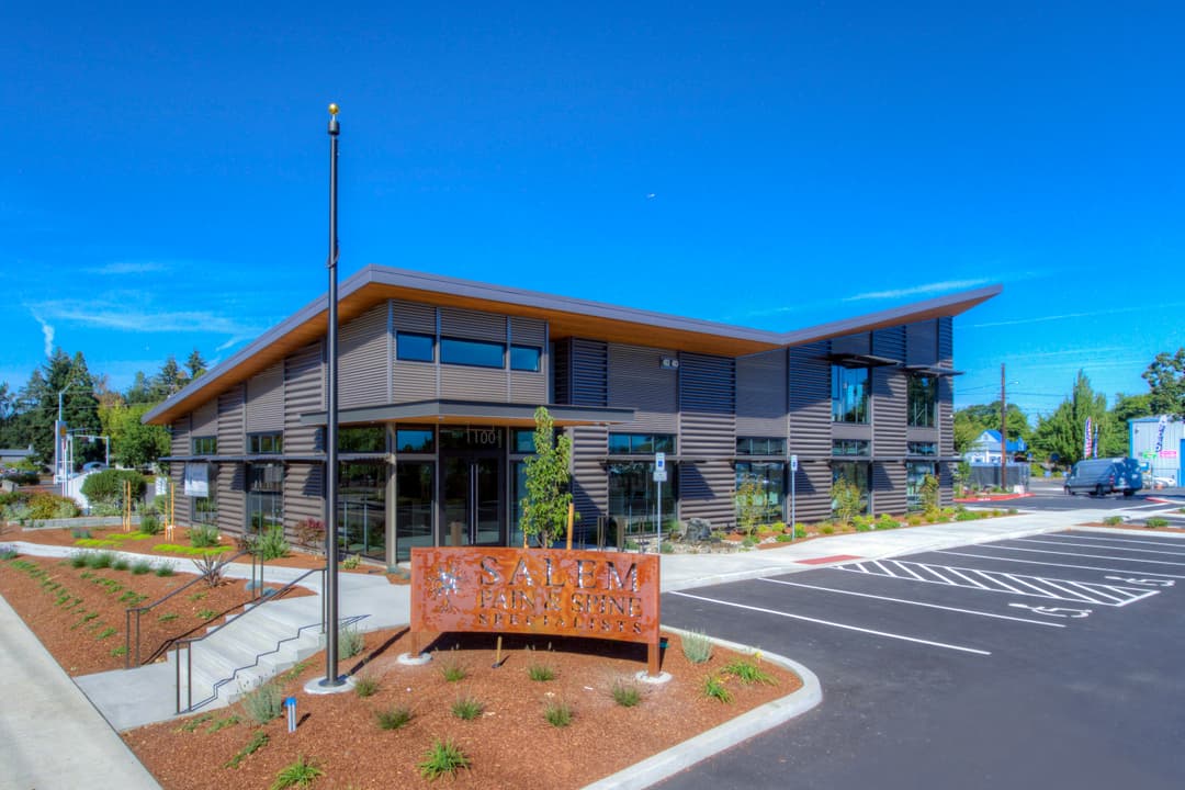 Modern building of Salem Farmers Market with landscaped parking area and clear blue sky.