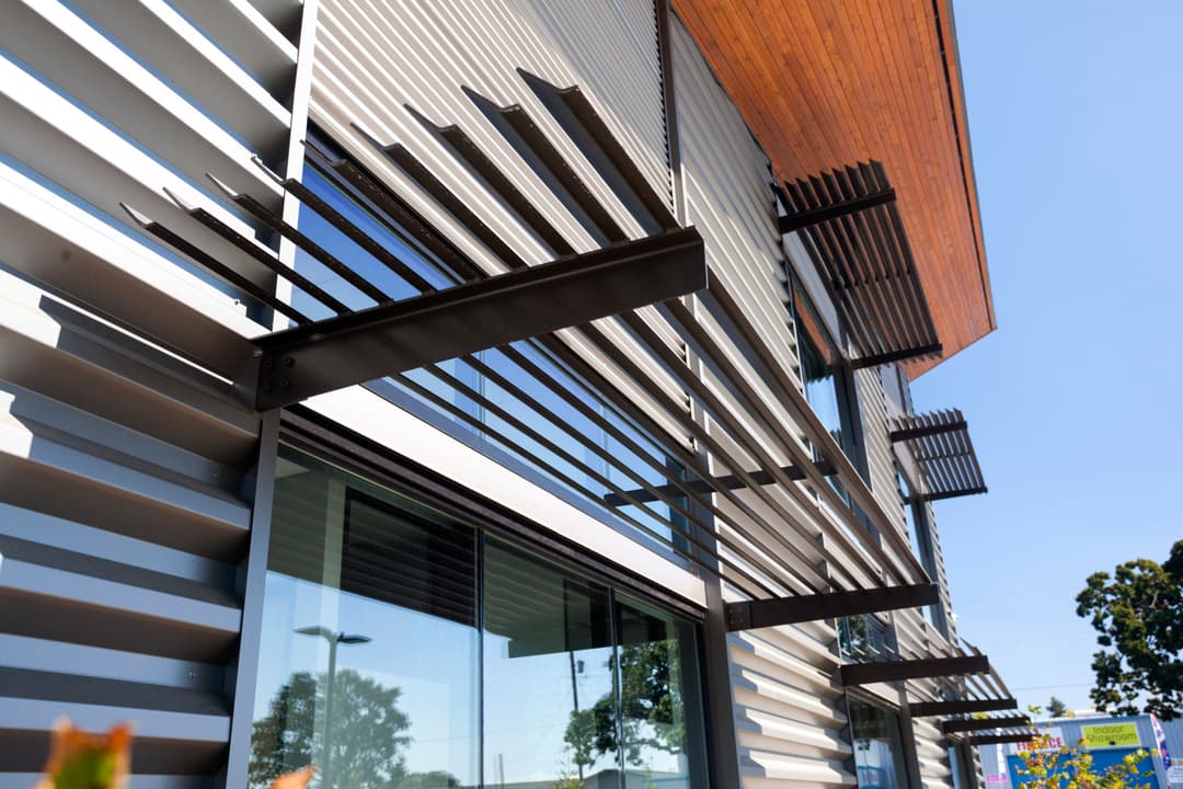 Modern building facade featuring sleek metal slats and large windows against a clear blue sky.