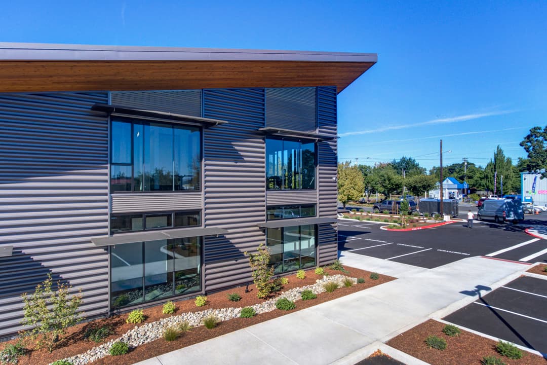 Modern commercial building with large windows, landscaped surroundings, and clear blue sky.