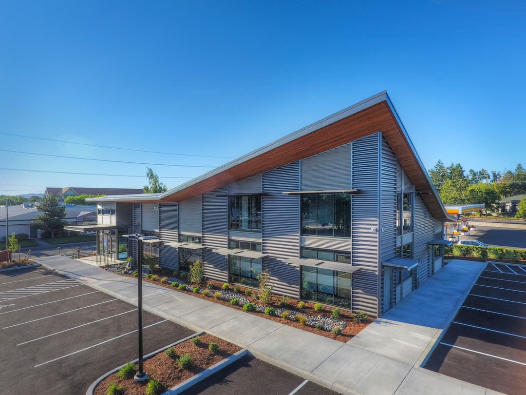 Modern office building with angular design, large windows, and landscaped parking lot.
