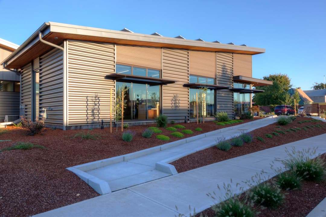 Modern building with sleek design, large windows, and landscaped pathway. Eco-friendly architecture.