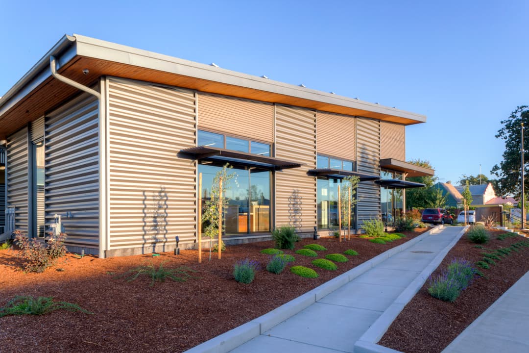 Modern commercial building with large windows and landscaped pathway. Sustainable design features.