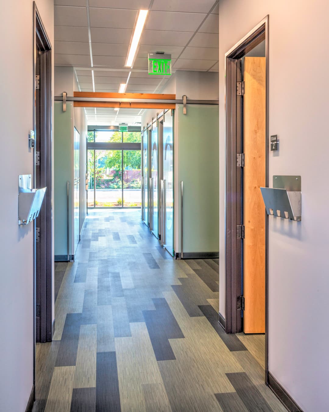 Modern office hallway with glass doors, natural light, and sleek flooring.