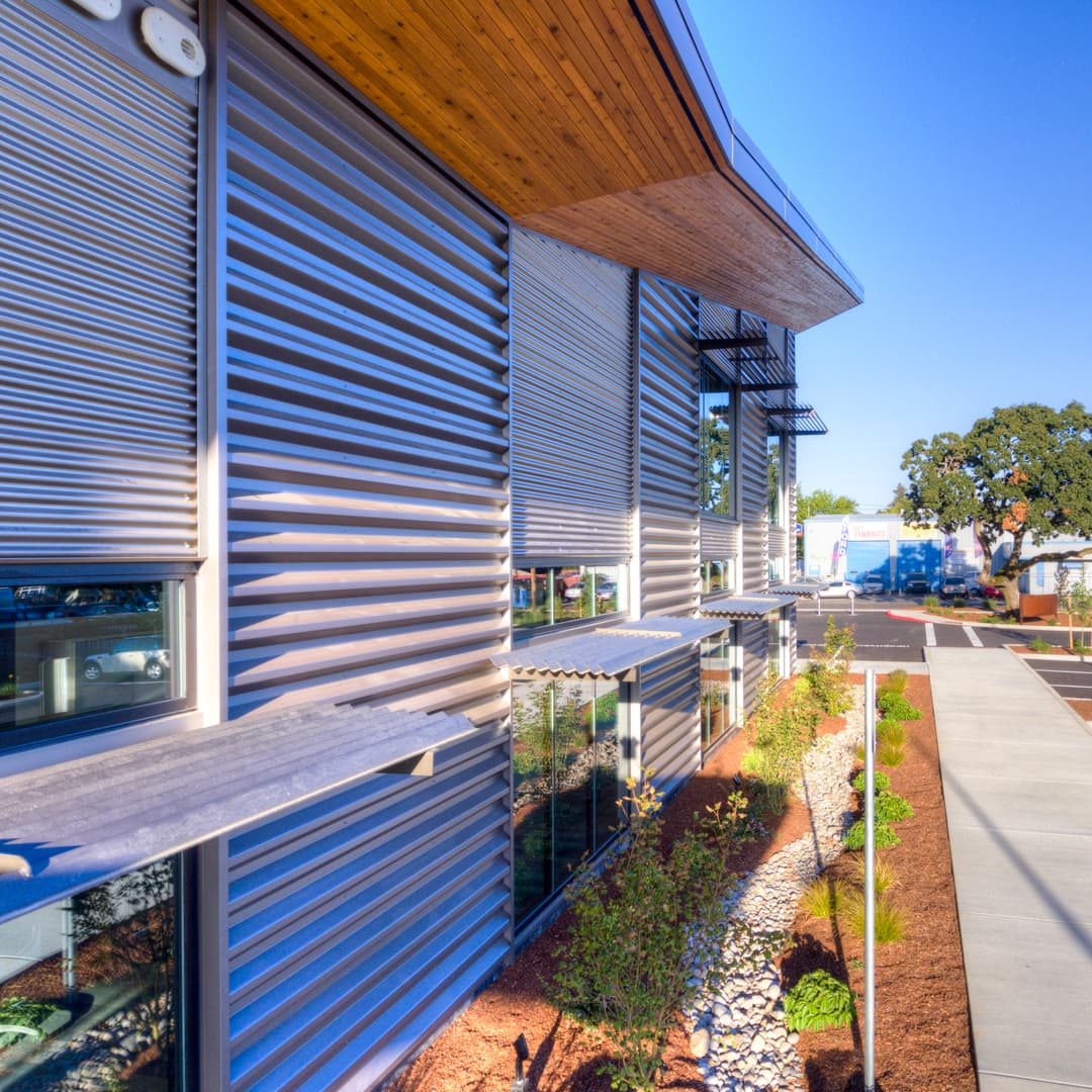 Modern architectural facade with metal cladding and landscaped path in bright sunlight.