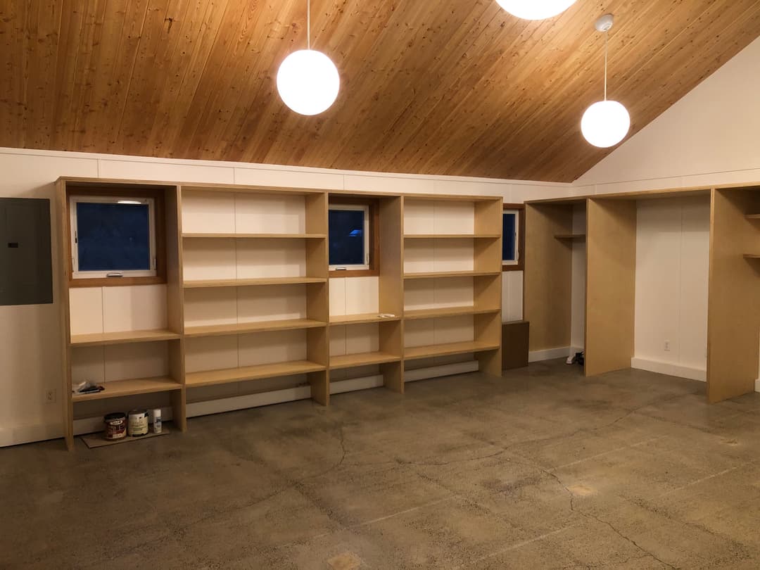 Empty room with wooden ceiling, two light fixtures, and custom built-in shelves against the walls.
