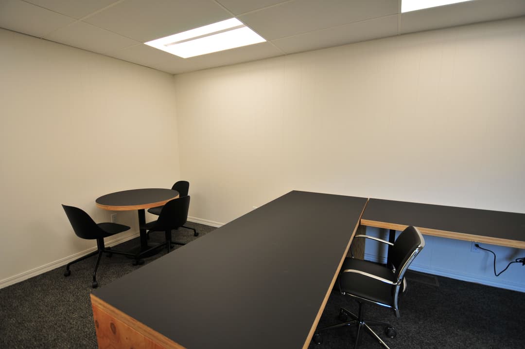 Empty office space featuring a large desk, round table, and black chairs. Modern and minimalistic design.