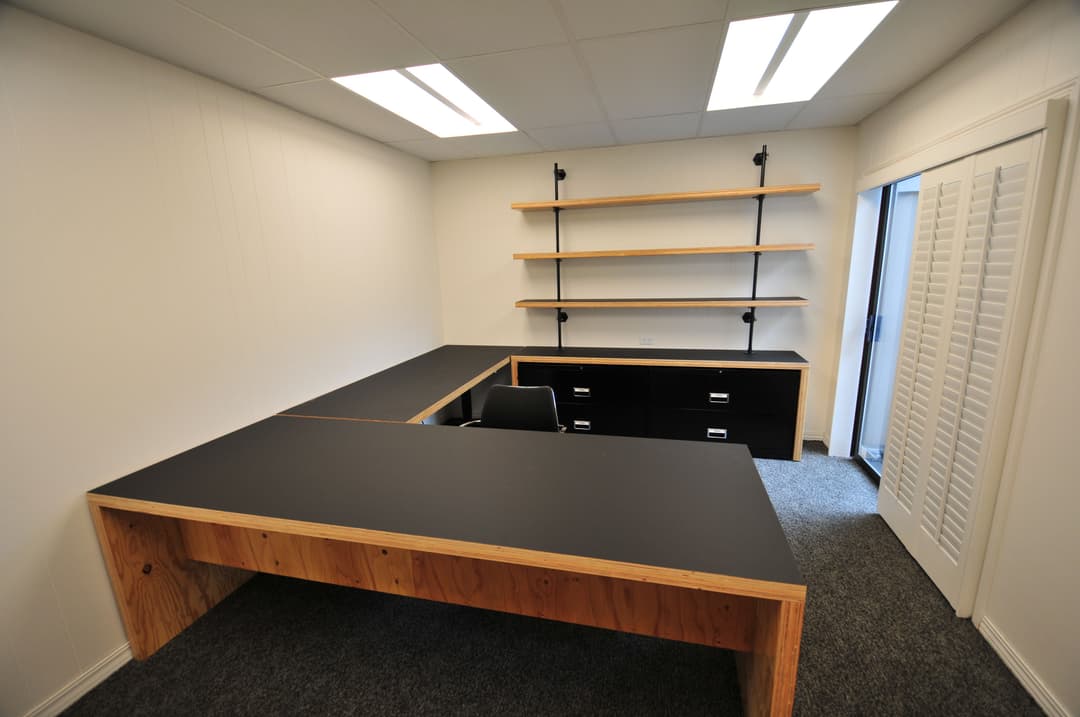 Modern office setup with a large black desk, shelving, and file drawers in a bright space.