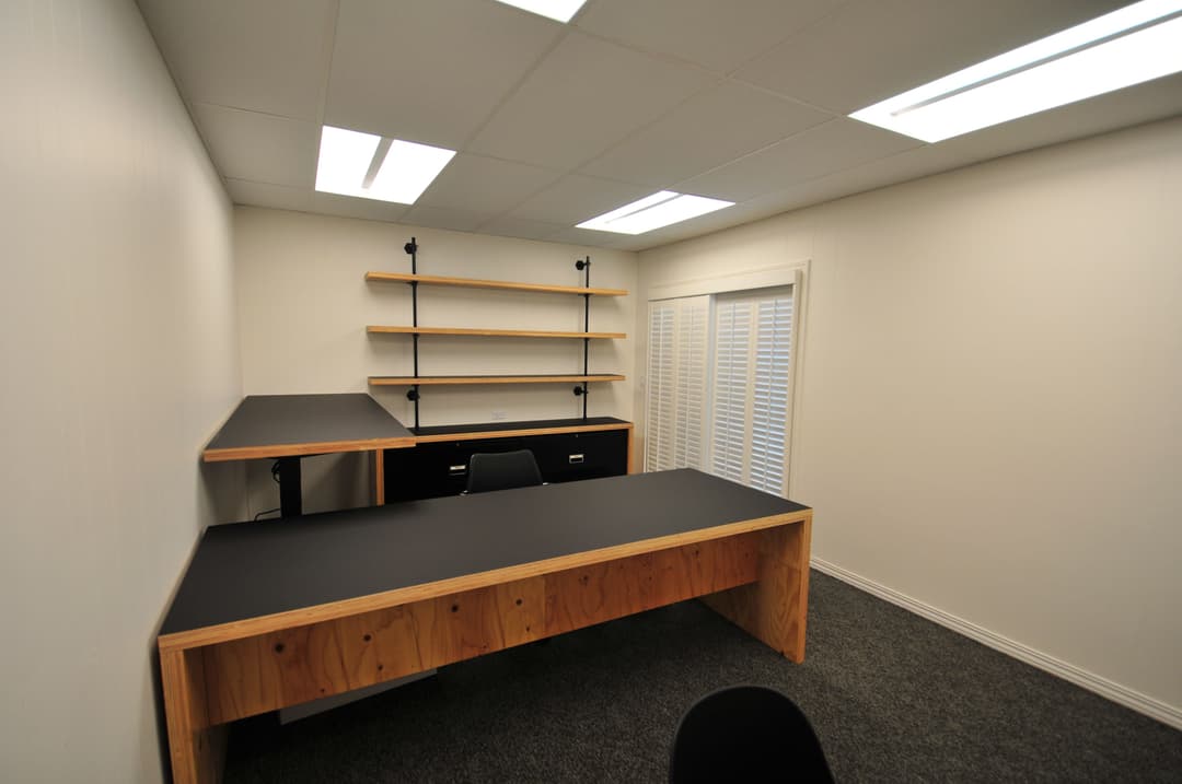 Modern home office setup with wooden desk, black shelving, and bright lighting.