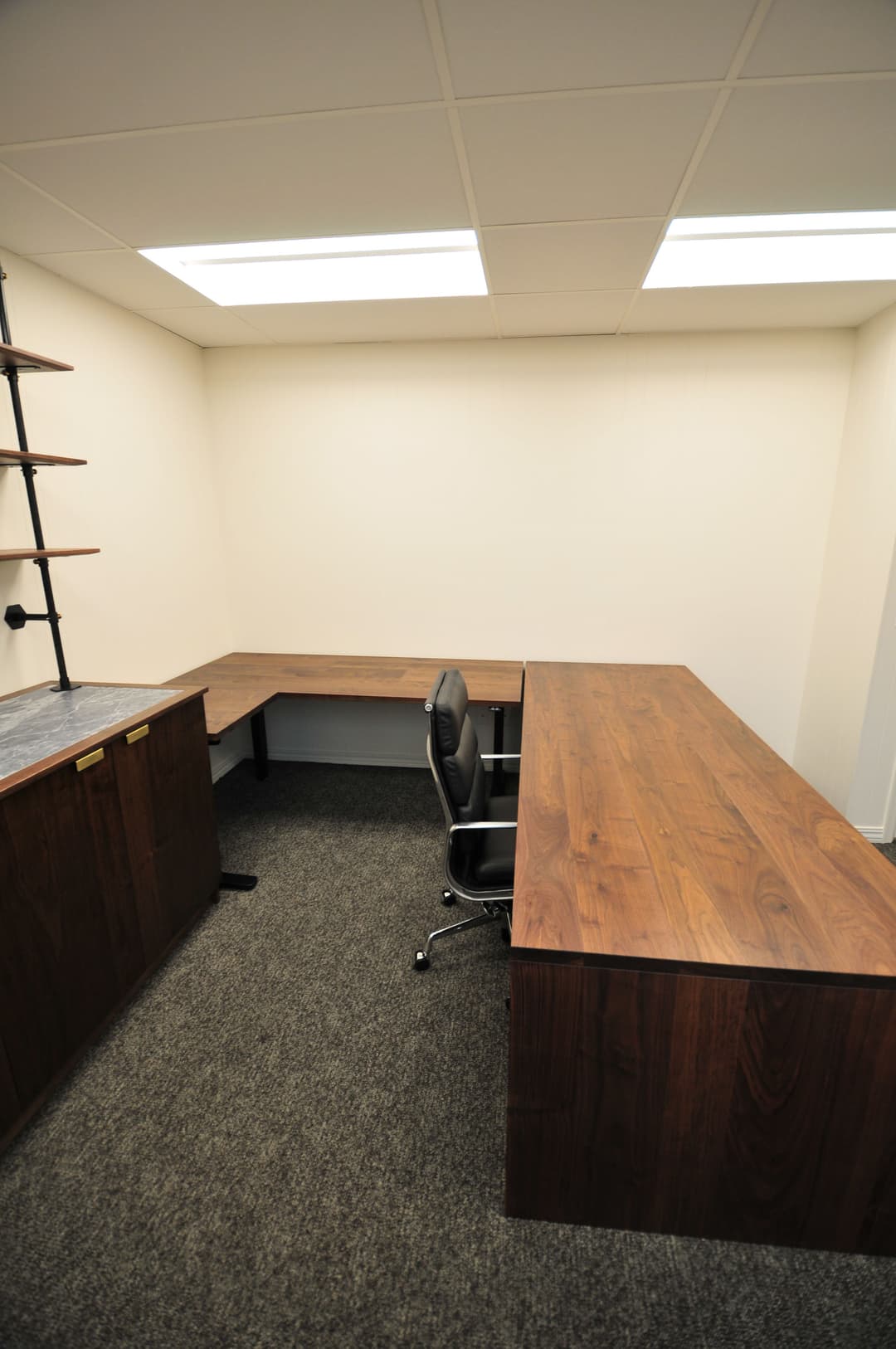 Modern office space with wooden desks, black chair, and carpeted floor. Ideal for productivity.