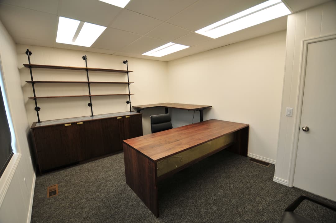Modern office interior with a wooden desk, shelving unit, and carpeted flooring.