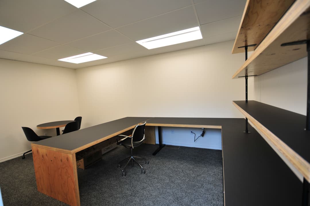 Modern office interior with a large desk, ergonomic chair, and minimalist shelving.