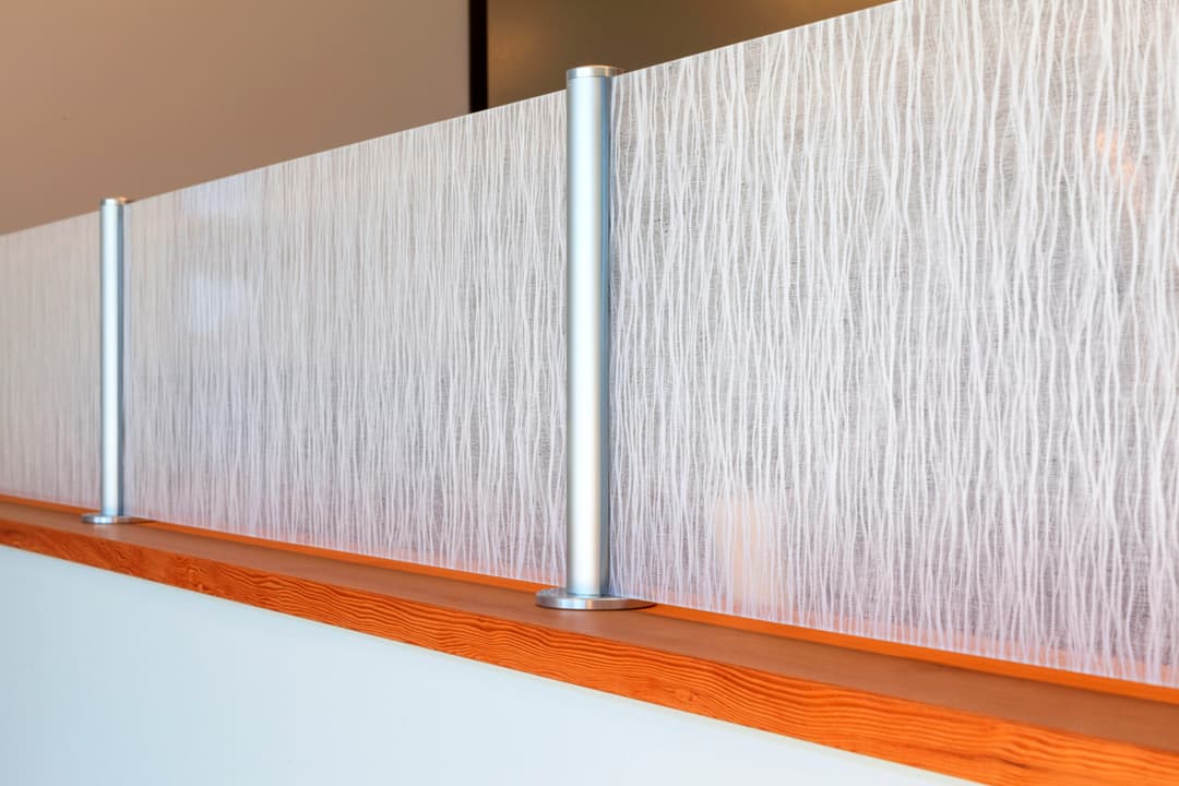 Modern frosted glass divider with sleek metal posts and wooden base in contemporary interior.