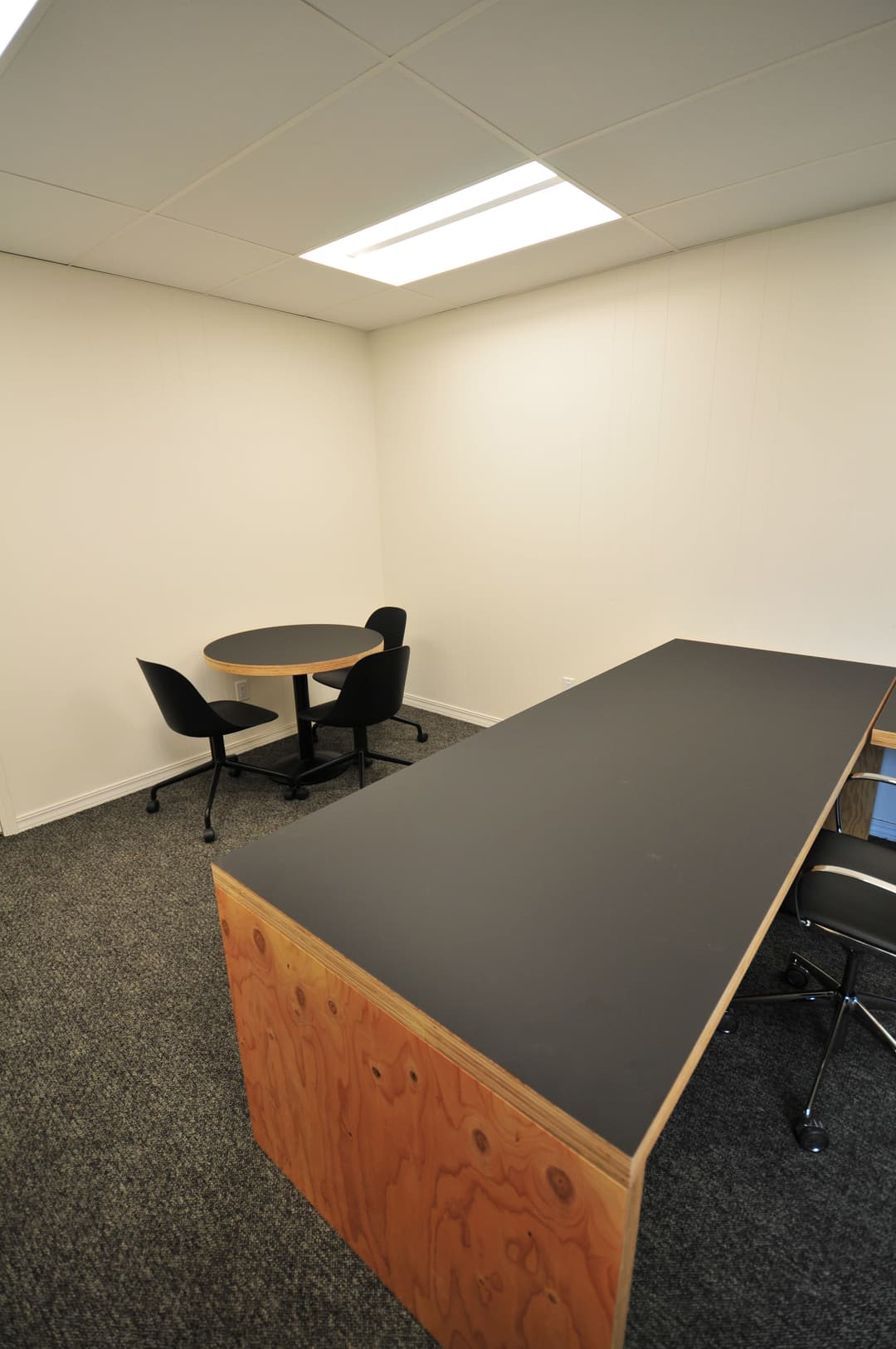 Minimalist office space featuring a round table, chairs, and a long desk in a bright environment.