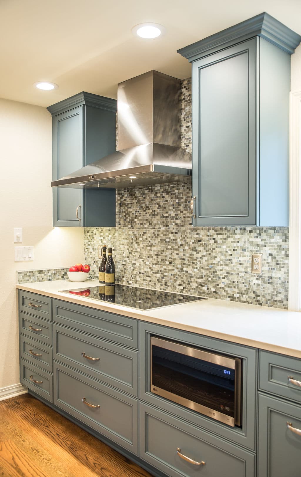 Modern kitchen with blue cabinets, mosaic backsplash, stainless steel hood, and a wine fridge.