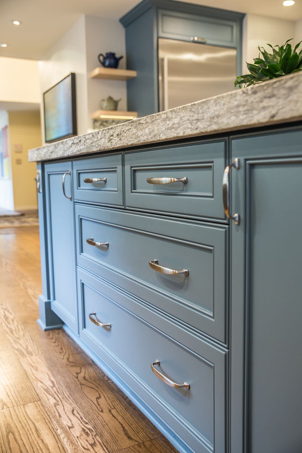 Blue kitchen island with granite countertop and modern silver handles on drawers.
