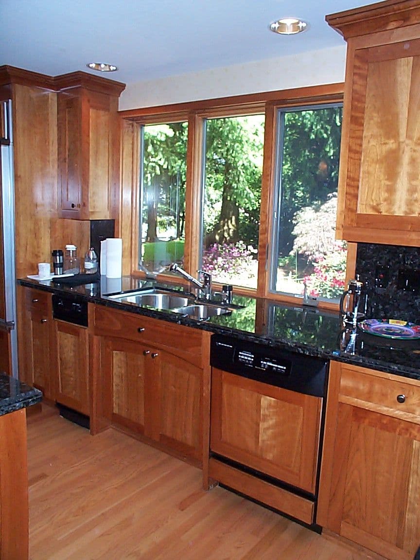 Modern kitchen with wood cabinets, granite countertops, and large windows overlooking a garden.