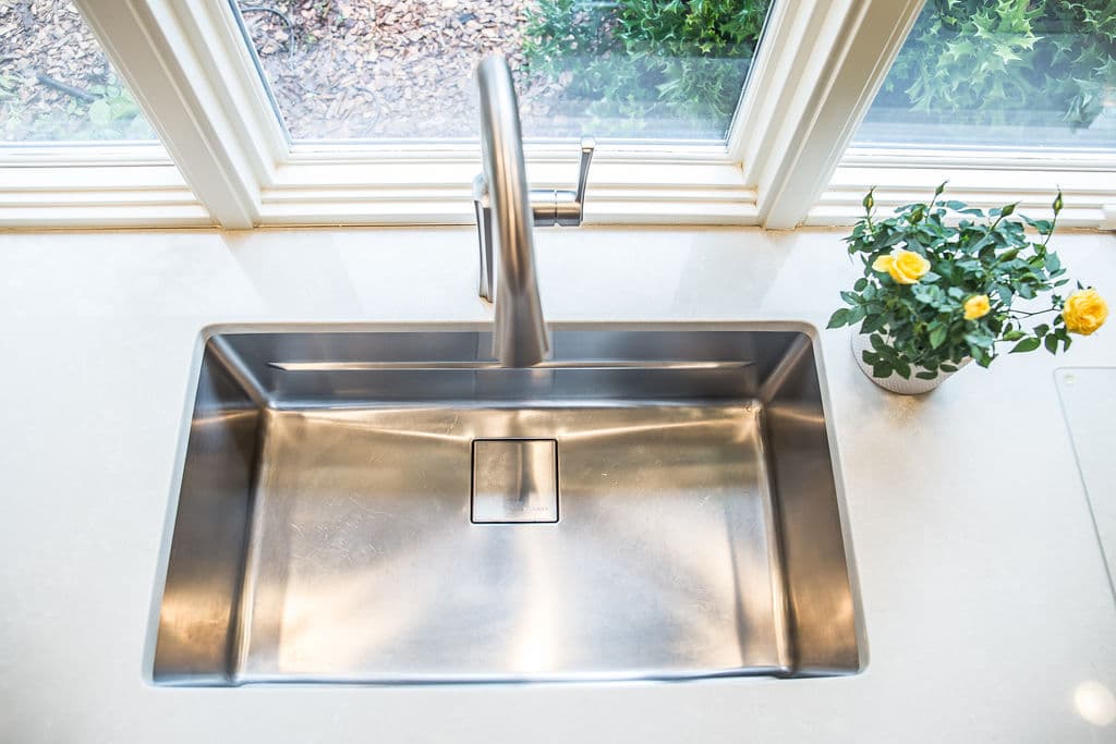 Modern stainless steel kitchen sink with a sleek faucet and a potted yellow flower.