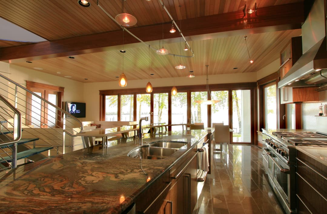 Modern kitchen with granite countertops, wood ceiling, and large windows overlooking nature.