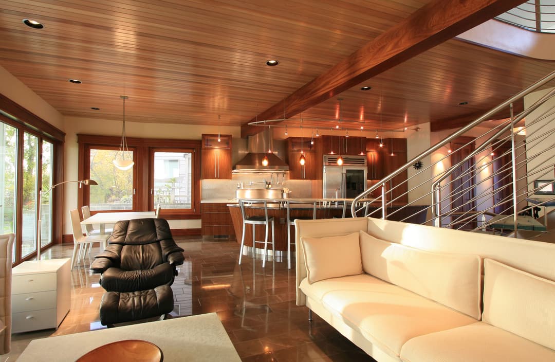 Modern open-concept living area with kitchen, stylish furniture, and wooden ceiling details.