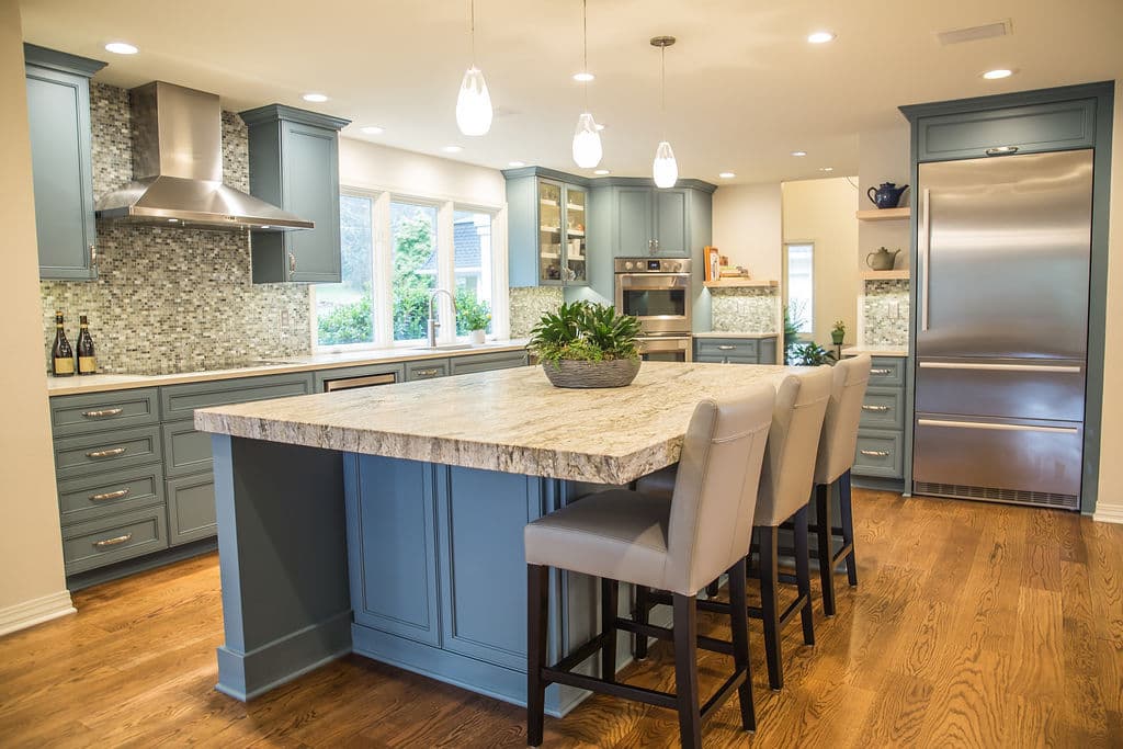 Modern kitchen with blue cabinetry, granite island, and stainless steel appliances. Bright and spacious.