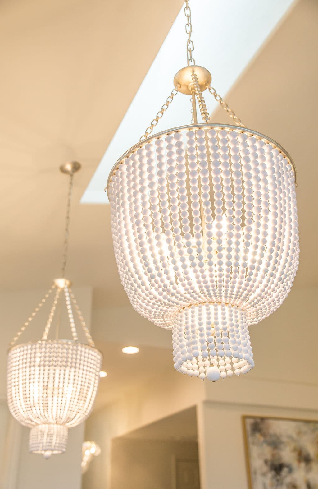 Elegant white bead chandeliers hanging from a ceiling, illuminating a modern interior space.