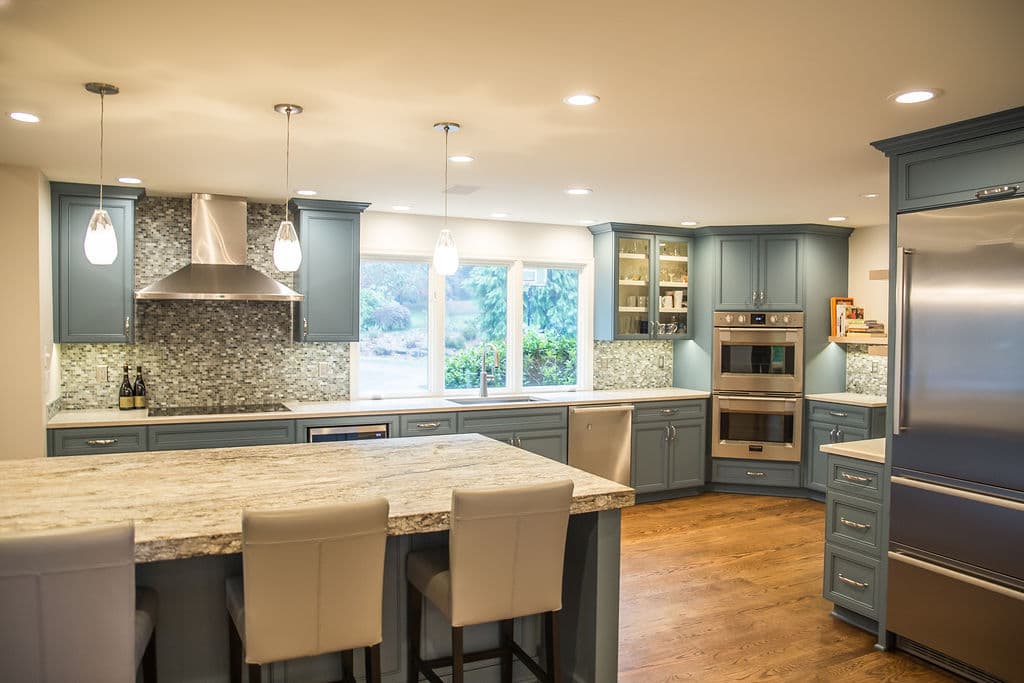 Modern kitchen with blue cabinets, granite island, stainless steel appliances, and natural light.