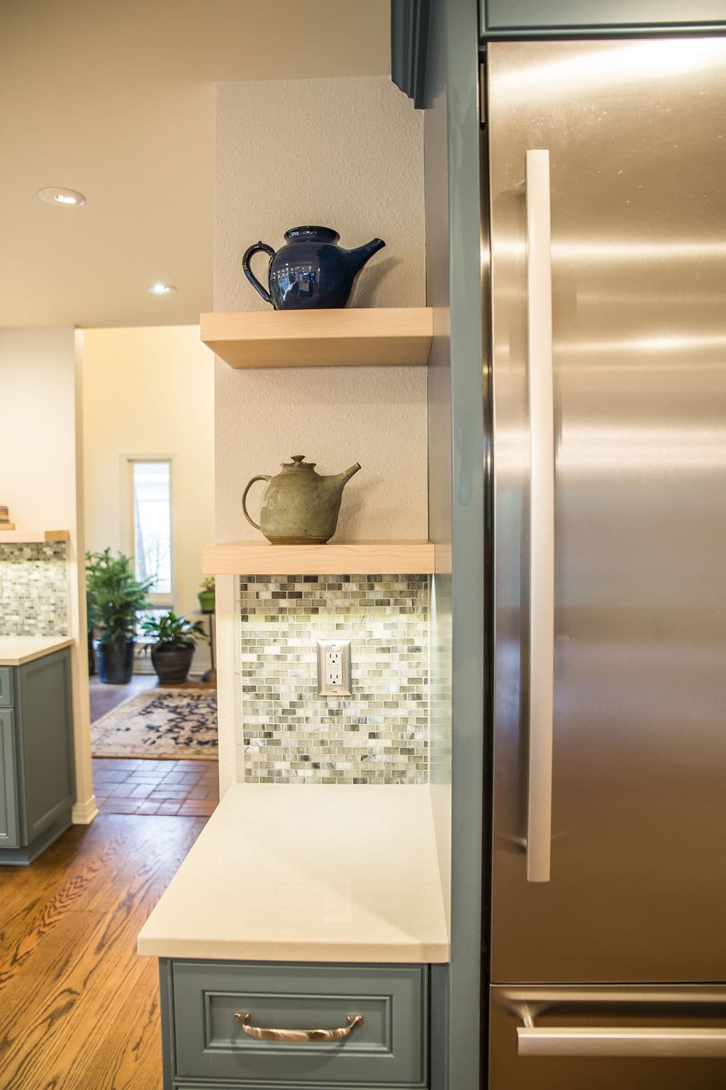 Modern kitchen corner featuring blue and green teapots on shelves beside stainless steel fridge.
