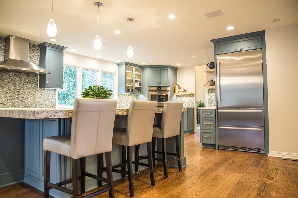 Modern kitchen with blue cabinets, granite countertops, and bar seating under pendant lights.