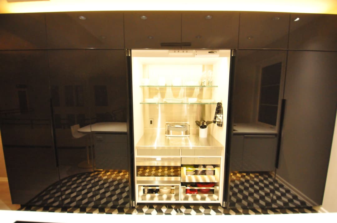 Modern kitchen with sleek black cabinetry and a stylish, illuminated refrigerator design.