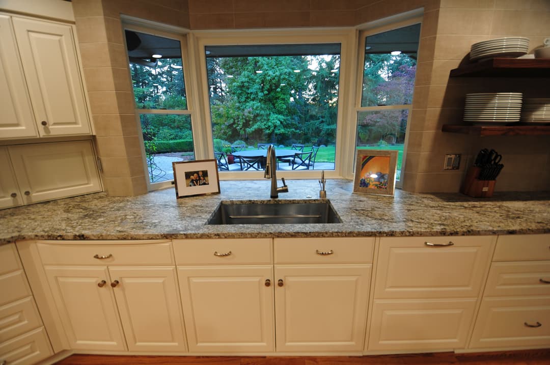 Modern kitchen sink with granite countertop and large window overlooking a lush garden.